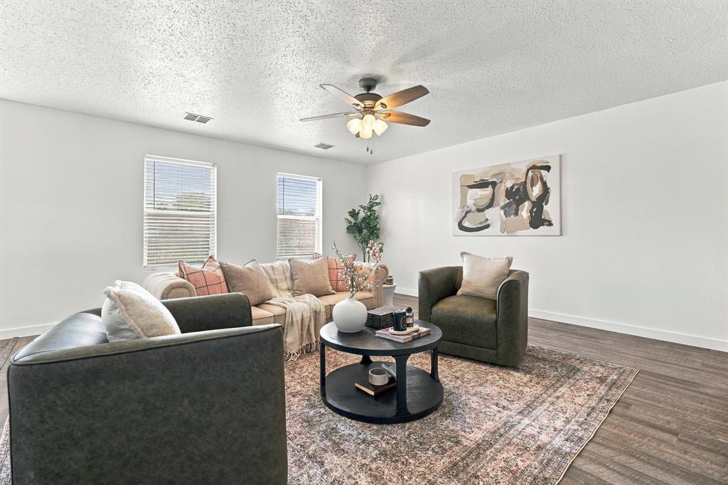 Living area featuring wood-finish flooring, two dual-pane windows with horizontal blinds, and a central ceiling fan with integrated lighting