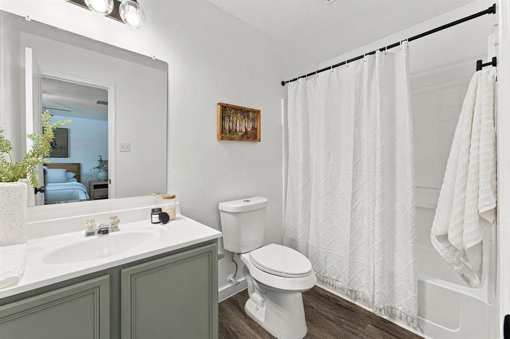 Bathroom featuring a vanity with a solid surface countertop, an integrated sink, a large wall-mounted mirror, wood-finish flooring, and a shower-tub combination with a wall surround