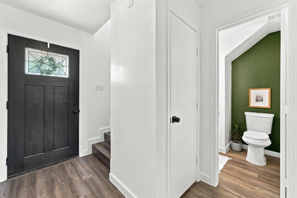 Entryway featuring a black solid-core front door with a decorative glass inlay, wood-finish flooring, a built-in storage closet, and a powder room with a white dual-flush toilet