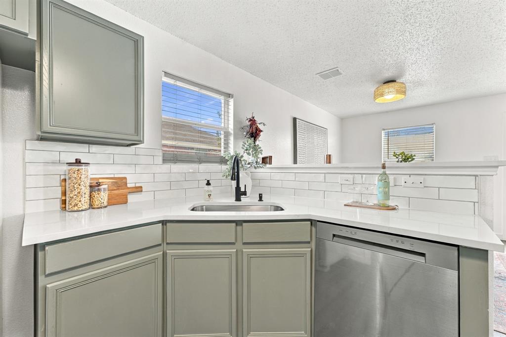 Kitchen featuring sage-toned cabinetry, white stone-composite countertops, subway tile backsplash, stainless steel dishwasher, and a matte black gooseneck faucet
