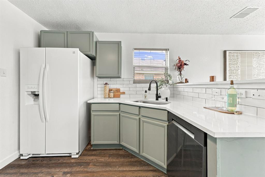 Kitchen featuring sage green cabinetry, white quartz countertops, white subway tile backsplash, stainless steel undermount sink with a matte black faucet, and wood-finish flooring