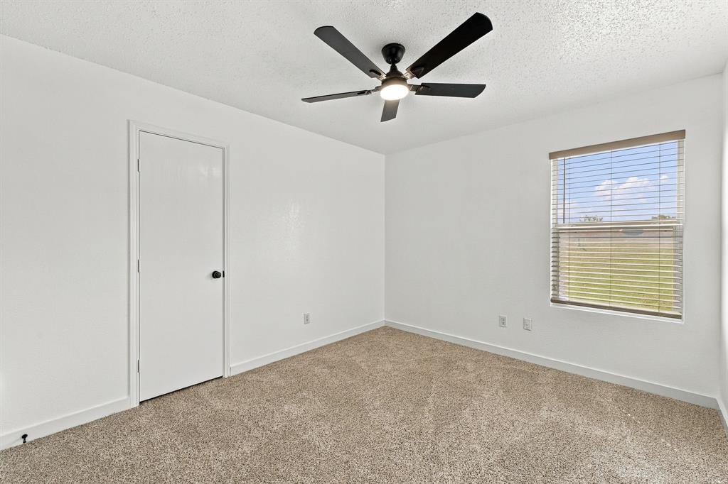 Neutral-toned carpeting, matte black ceiling fan with integrated lighting, single-panel interior door, and window with horizontal blinds
