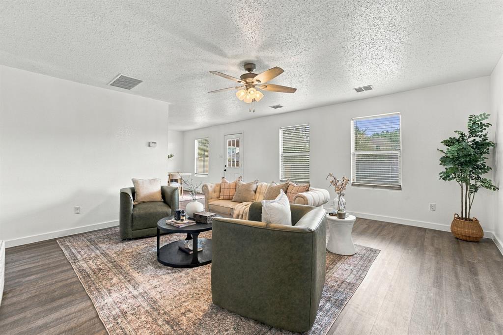 Open living area featuring wood-finish flooring, neutral walls, natural light through multiple windows, and a ceiling fan with integrated lighting