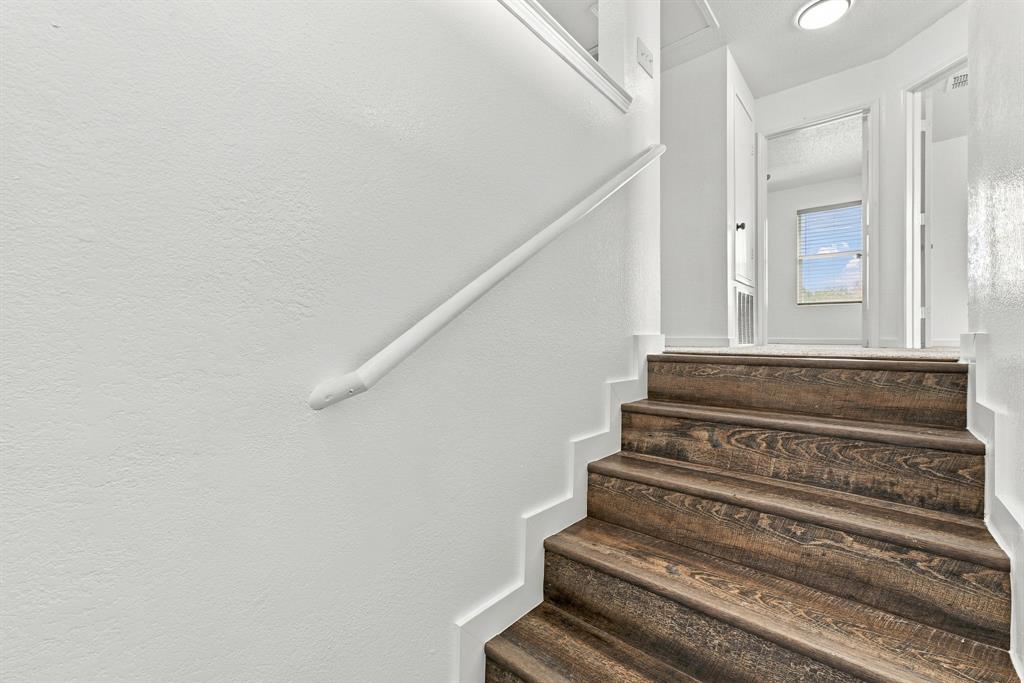 Staircase featuring wood-finish treads, white painted walls, and a matching handrail