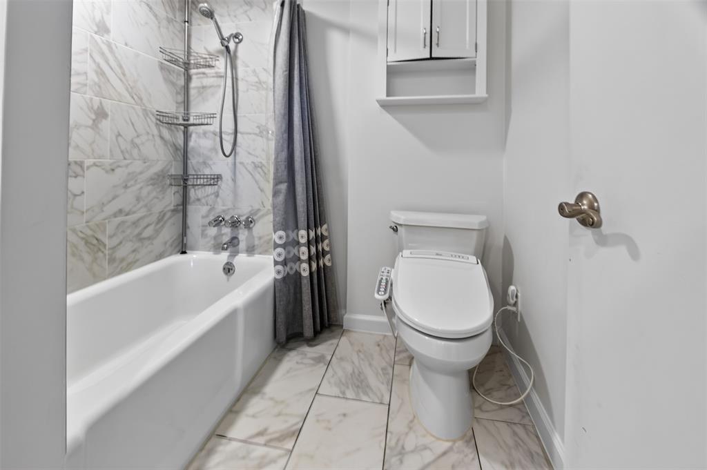 View of shower tub enclosure in Jack N Jill bath. Updated flooring and shower enclosure. Cabinet above Bidet. August 2026 wallpaper removed walls freshly painted.