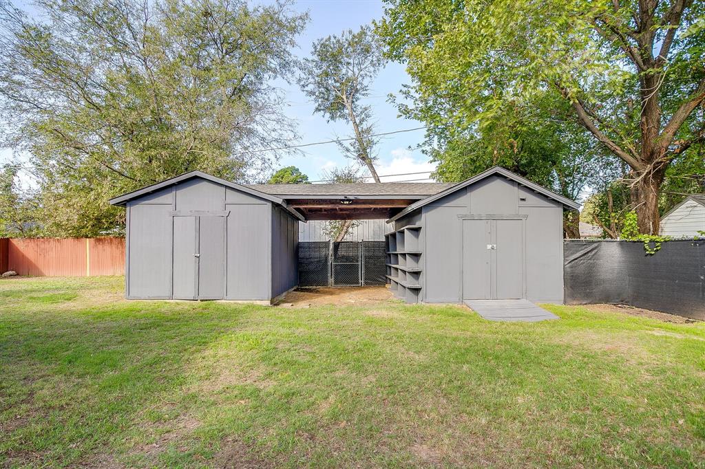 Dual-structure outdoor storage building featuring a central covered breezeway, built-in side shelving, and a ramped entry, situated on a fenced lot with mature trees