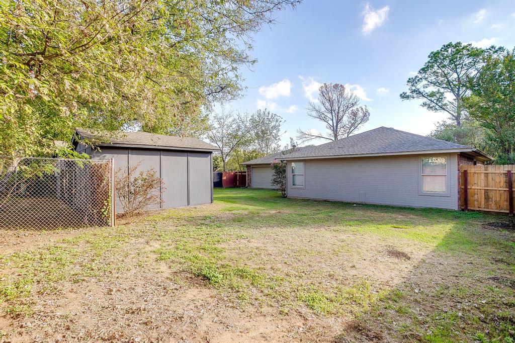 Expansive backyard featuring mature trees, a detached storage structure, chain-link fencing, and wood privacy fencing