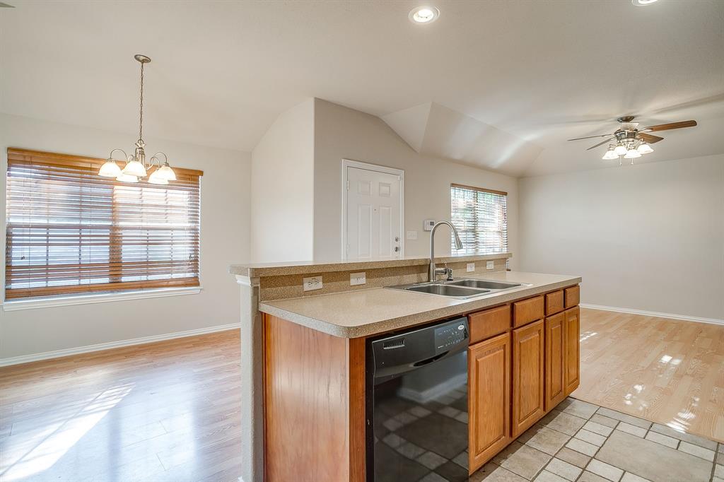 Kitchen island featuring wood cabinetry, a dual-basin stainless steel sink with a goose-neck faucet, and a dishwasher