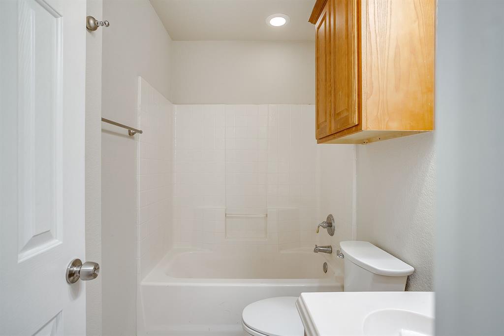 Full-size white bathtub with integrated surround, light-toned wood-finish cabinetry, recessed ceiling lighting, and a metal towel bar