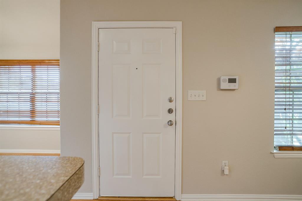 Six-panel entry door with integrated peephole, wall-mounted digital thermostat, and windows featuring horizontal blinds