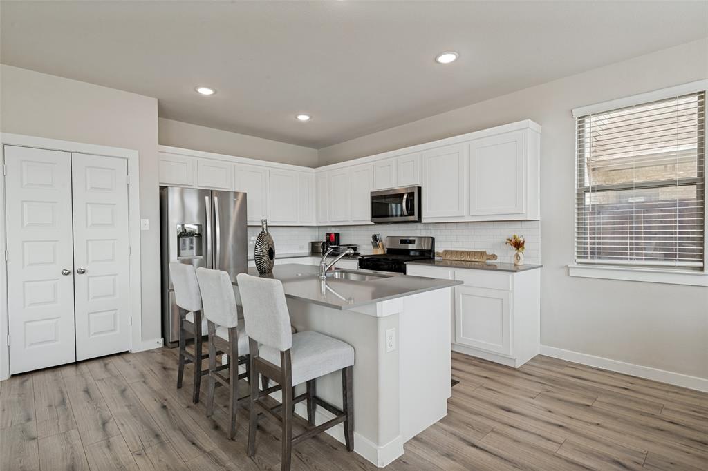 Kitchen featuring white cabinetry, solid-surface countertops, subway tile backsplash, stainless steel appliances, and wood-finish flooring Kitchen featuring white cabinetry, solid-surface countertops, subway tile backsplash, stainless steel appliances, and wood-finish flooring