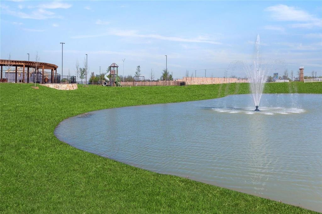 Manicured green space featuring a pond with a central fountain, pergola structure, playground equipment, and perimeter stone wall