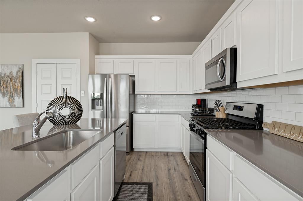 Kitchen featuring white Shaker-style cabinetry, quartz countertops, a white subway tile backsplash, stainless steel appliances, and wood-finish flooring Kitchen featuring white Shaker-style cabinetry, quartz countertops, a white subway tile backsplash, stainless steel appliances, and wood-finish flooring