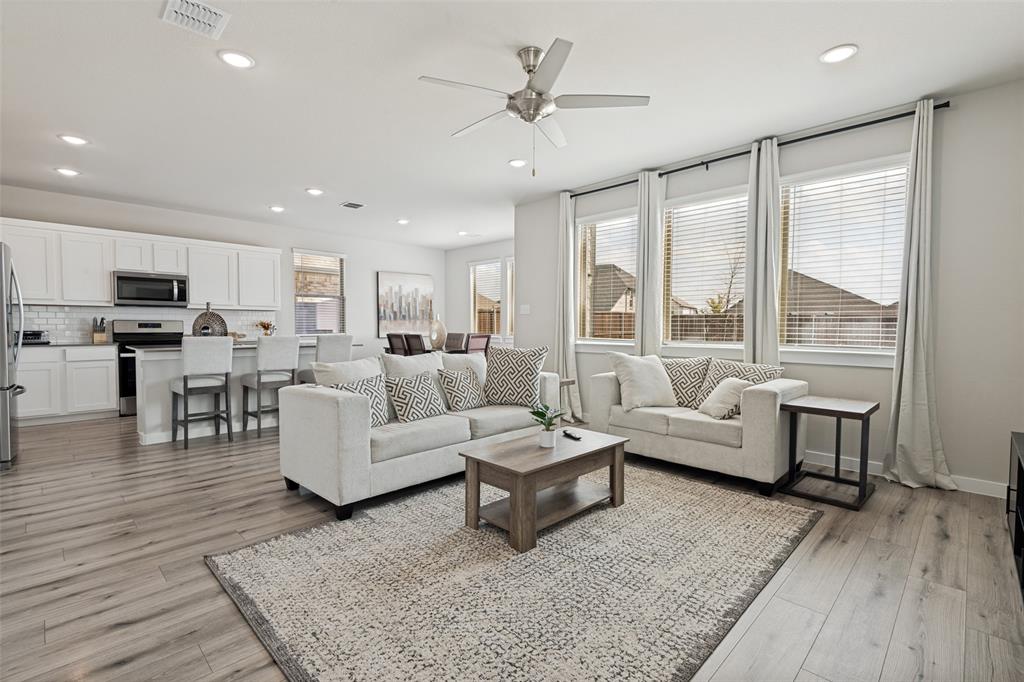 Open-concept main room featuring wood-finish flooring, recessed lighting, a brushed-nickel ceiling fan, and large windows with horizontal blinds Open-concept main room featuring wood-finish flooring, recessed lighting, a brushed-nickel ceiling fan, and large windows with horizontal blinds