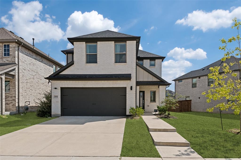 Two-story residence featuring a light-toned brick facade, dark-finish garage door, concrete driveway, and covered entryway Two-story residence featuring a light-toned brick facade, dark-finish garage door, concrete driveway, and covered entryway