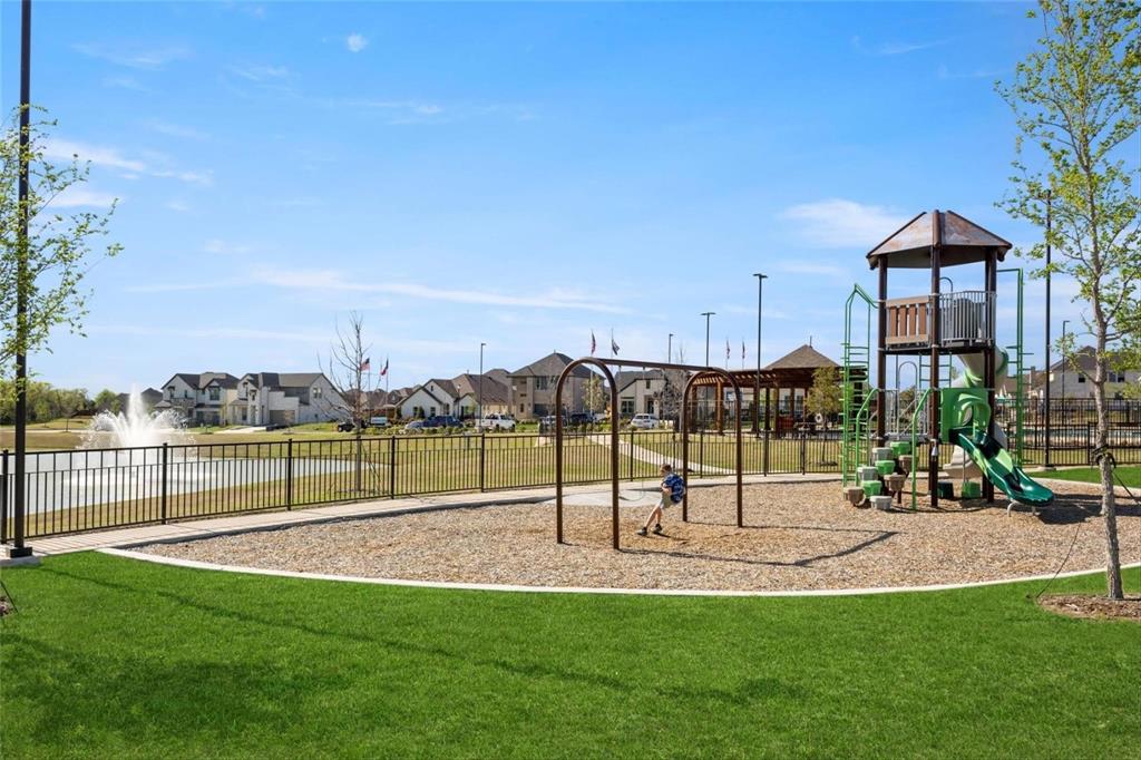 Community recreational area featuring a playground with a tower structure and swings, a water fountain feature, and a pergola