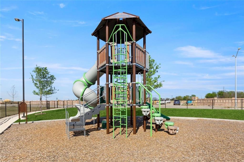 Multi-level playground structure featuring a spiral slide, vertical climbing ladder, and integrated stairs, set within a manicured area with wood-chip ground cover and perimeter metal fencing