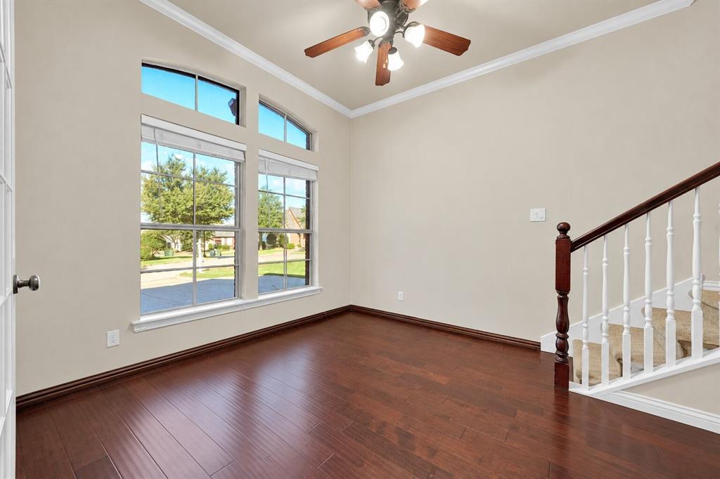 High-ceiling room featuring dark wood-finish flooring, tall arched windows, a multi-light ceiling fan, and a staircase with a stained wood handrail and white balusters
