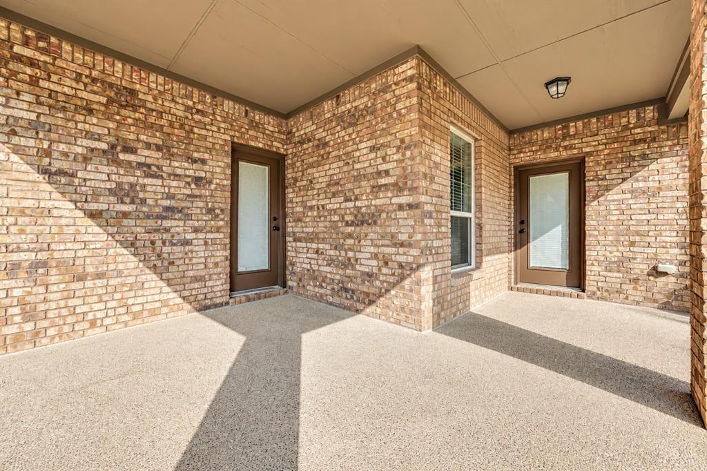 Covered patio featuring red brick masonry, aggregate concrete flooring, two glass-paneled exterior doors, and a flush-mount overhead light fixture