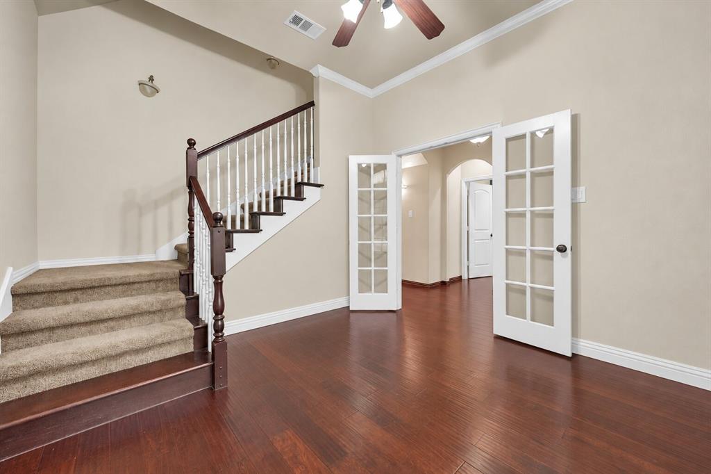 Vaulted ceilings, wood-finish flooring, staircase with a stained-wood banister, white-paned French doors, and decorative crown molding