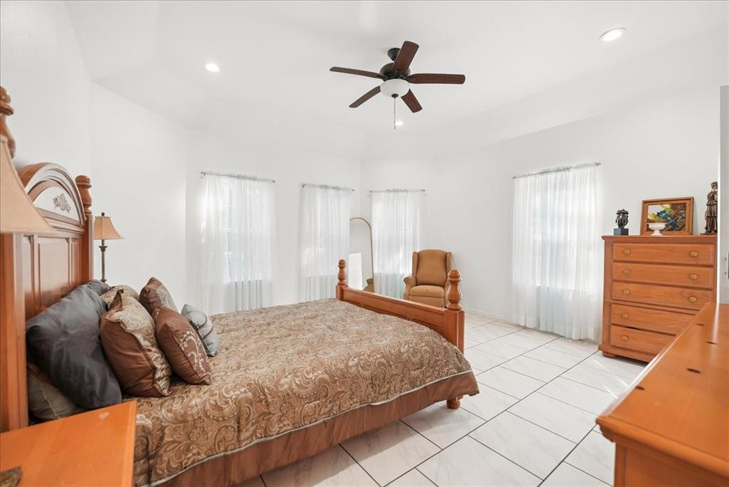 Vaulted ceiling featuring a central multi-blade ceiling fan and recessed lighting, finished with tile flooring and multiple windows