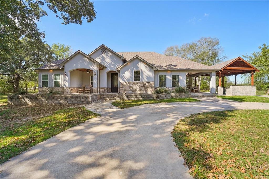 Single-story residence with a stone and stucco facade, concrete driveway, covered porch, and attached outdoor living structure with a stone-finish built-in counter