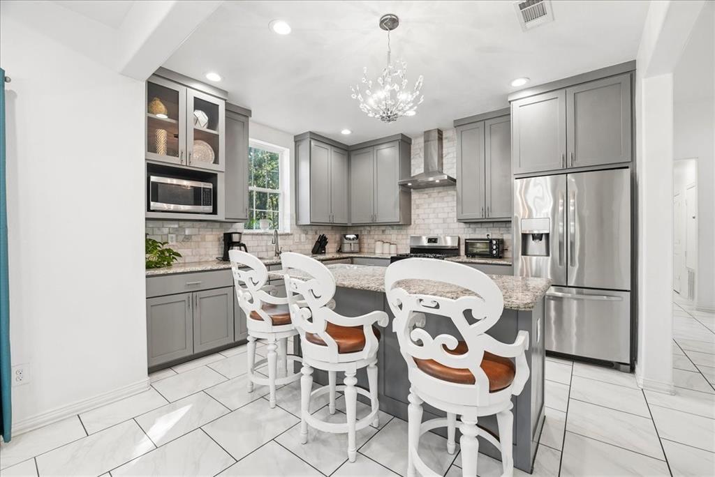 Kitchen featuring grey shaker-style cabinetry, stone-surface countertops, subway tile backsplash, stainless steel appliances, and tile flooring