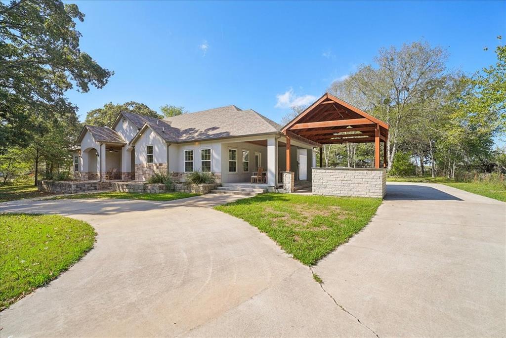 Exterior featuring masonry cladding, a concrete driveway, a covered patio, and a detached open-air pavilion with a stone-finished base