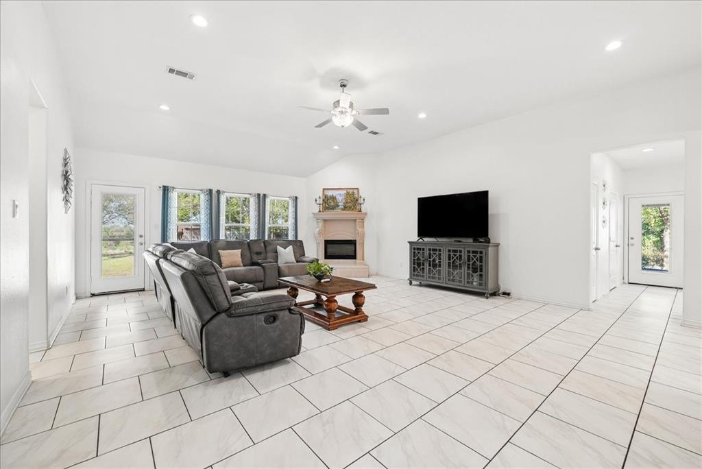 Vaulted ceilings, large-format tile flooring, a corner fireplace with a decorative mantel, multiple windows with natural light, and recessed lighting