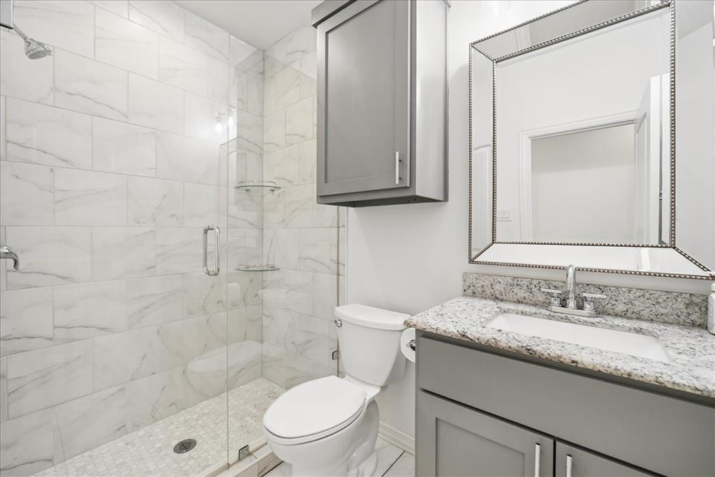 Walk-in shower with floor-to-ceiling tile, grey shaker-style vanity, stone-finish countertop, under-mount sink, and wall-mounted storage cabinet