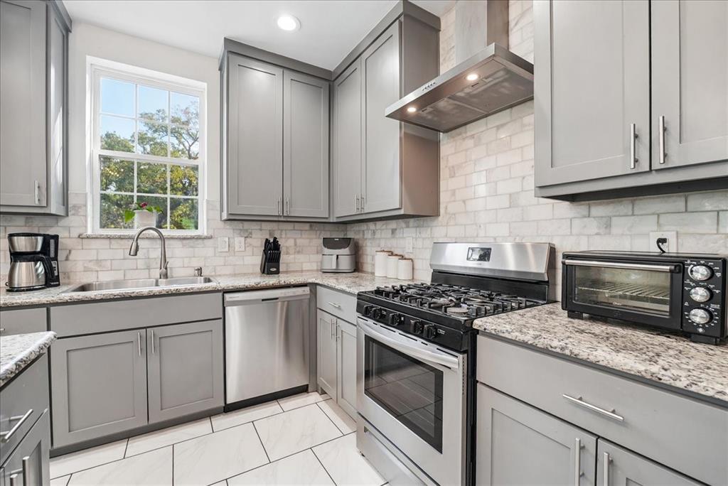Kitchen featuring grey shaker-style cabinetry, stainless steel appliances, stone-look countertops, a subway tile backsplash, and large-format floor tiles