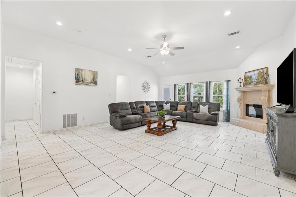 Living area featuring vaulted ceilings, neutral ceramic tile flooring, recessed lighting, and a decorative fireplace with a stone-finish surround