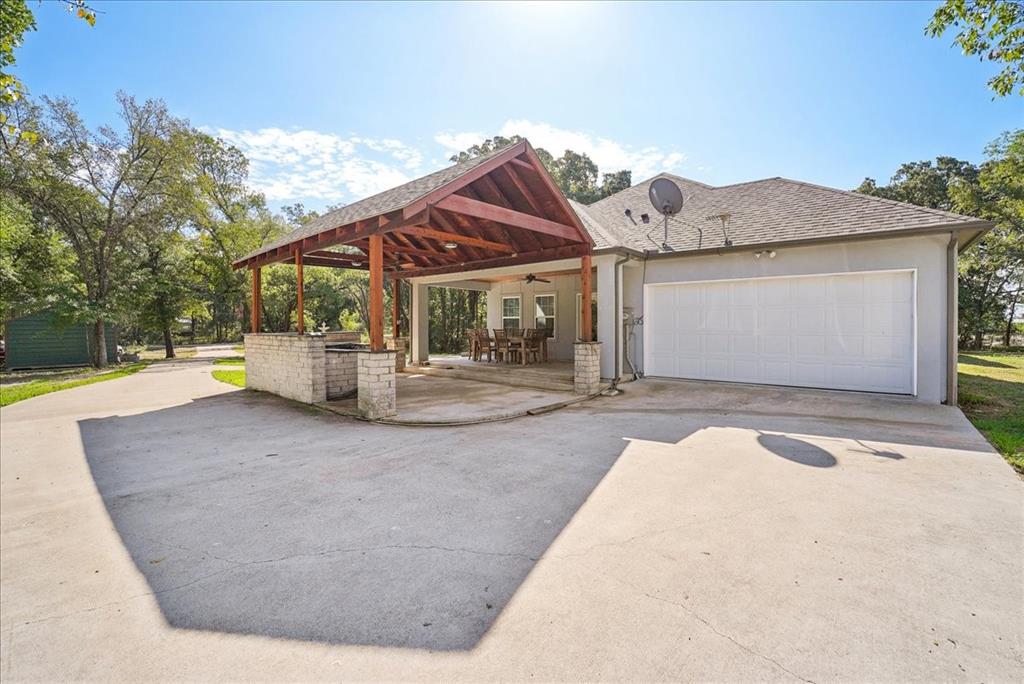 Covered outdoor pavilion featuring a stone-base prep area, wood-beam vaulted ceiling, integrated ceiling fan, and concrete patio