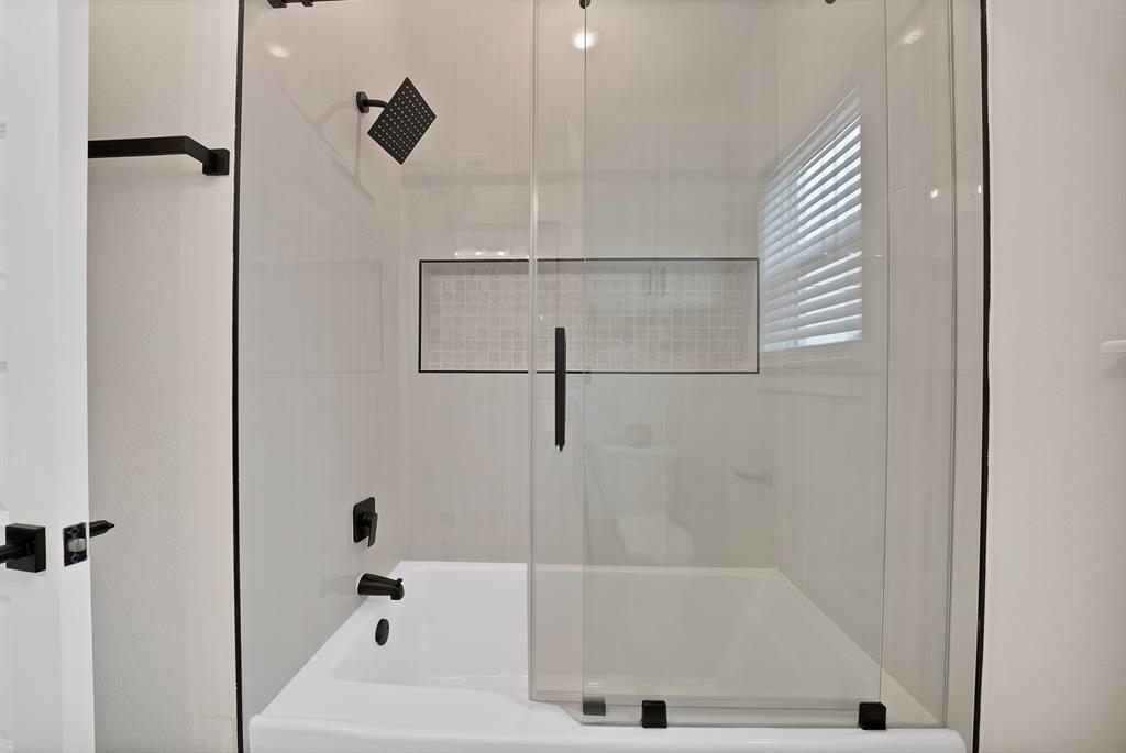 Bathtub and shower combination featuring white tiled surround, built-in recessed tiled niche, sliding glass door, and matte black hardware