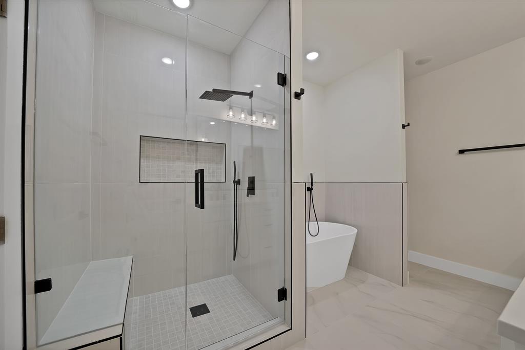 Walk-in shower featuring a frameless glass enclosure, built-in tiled bench, recessed niche, and matte black rainfall shower head, complemented by a freestanding soaking tub