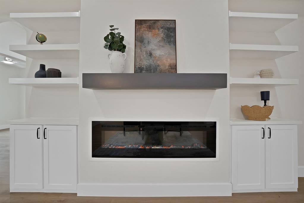 Linear electric fireplace featuring a dark surround, complemented by built-in lower cabinetry with matte black hardware and white floating shelving