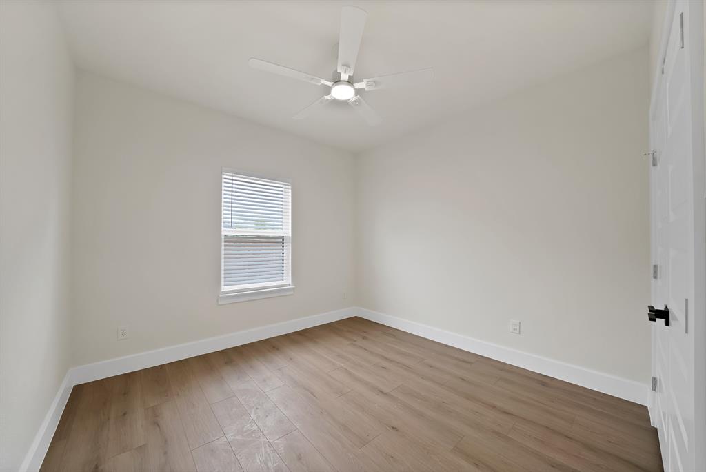 Interior room featuring wood-finish flooring, a neutral color palette, a central ceiling fan with integrated lighting, and a single-hung window with blinds