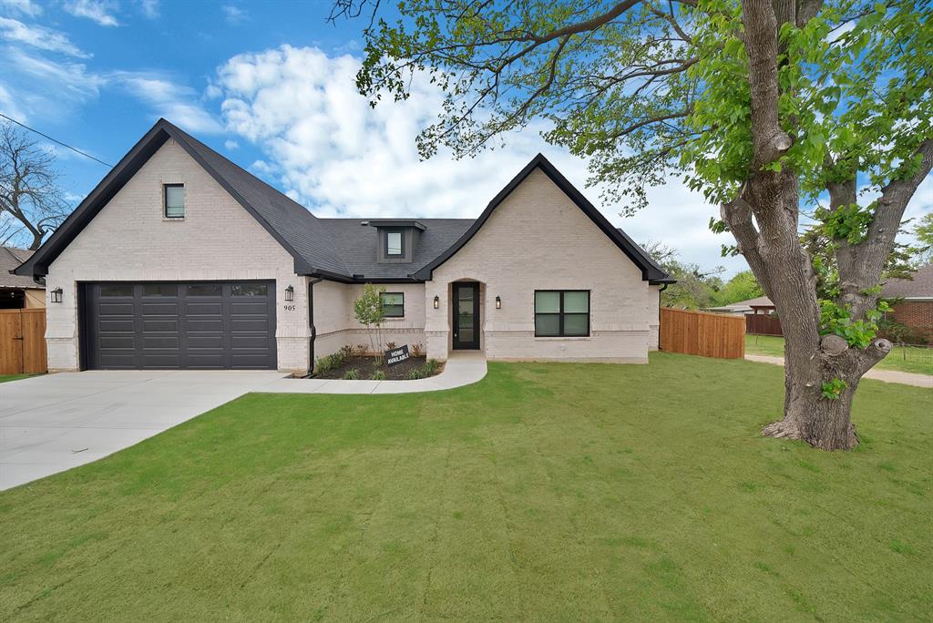 Painted brick exterior featuring a multi-gabled roofline, dark-toned garage door, concrete driveway, and mature landscaping