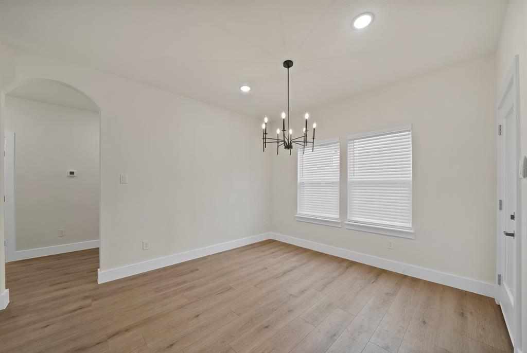 Interior space featuring wood-finish flooring, a multi-arm candle-style chandelier, recessed lighting, double windows with horizontal blinds, and a rounded archway