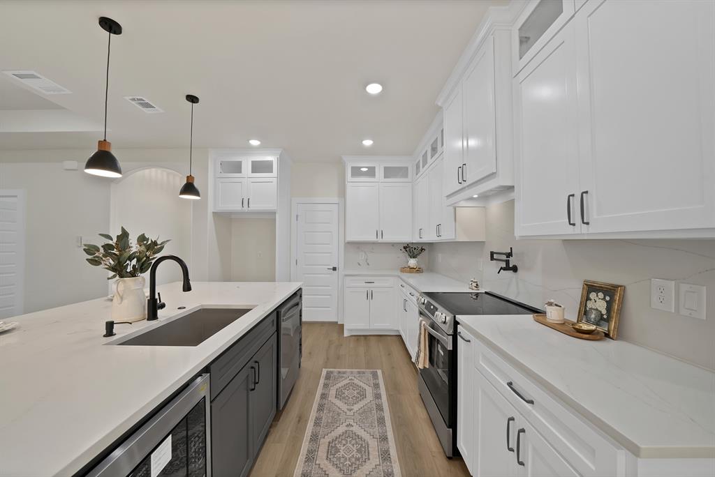 Kitchen featuring white shaker-style cabinetry with upper transom windows, stone-finish countertops, a contrasting dark-finish kitchen island with a farmhouse sink, wood-finish flooring, and pendant lighting