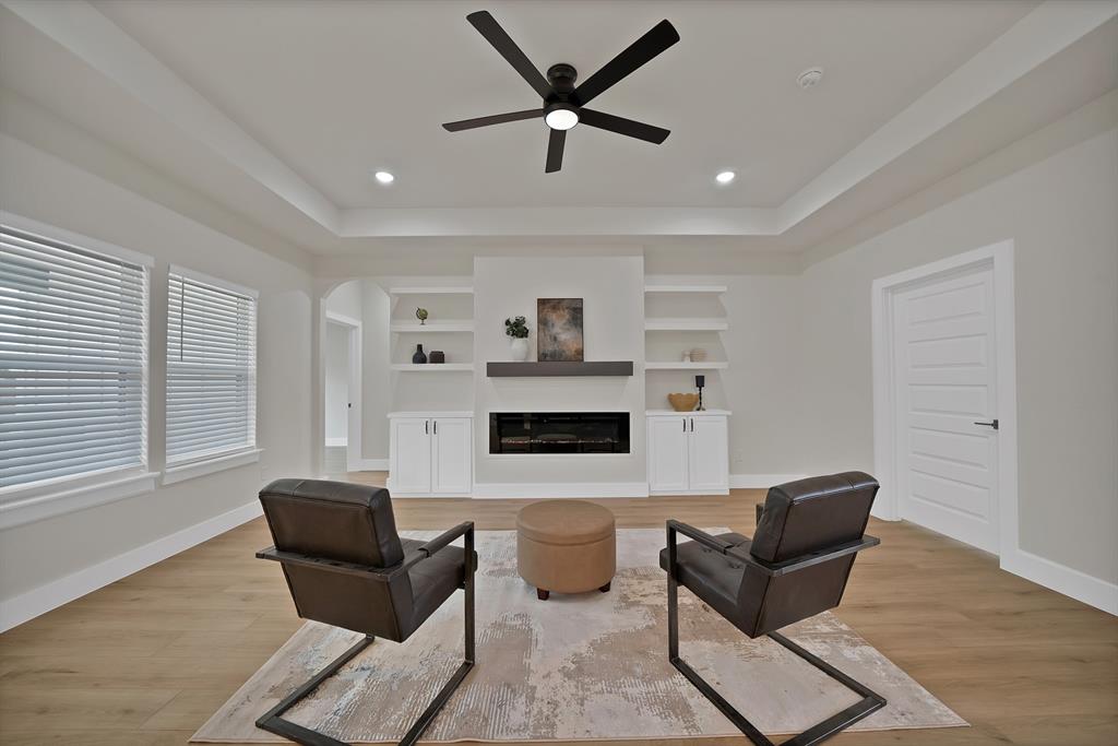 Living area featuring a tray ceiling, wood-finish flooring, built-in shelving, white cabinetry, and a linear fireplace with a mantel
