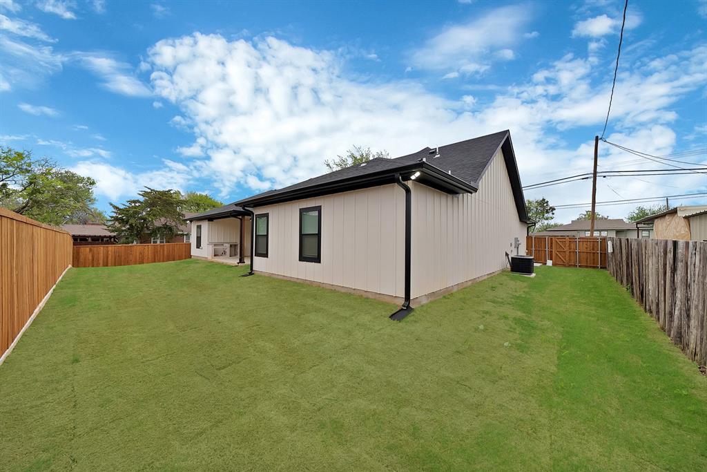 Expansive backyard featuring a sodded lawn, vertical board-and-batten siding, dark-framed windows, a pitched roofline, and full perimeter wood fencing