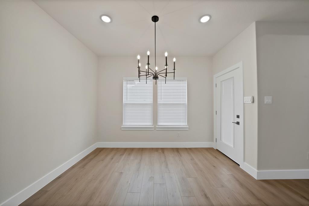 Room featuring wood-finish flooring, recessed lighting, a multi-arm candle-style chandelier, dual windows with integrated blinds, and a paneled entry door
