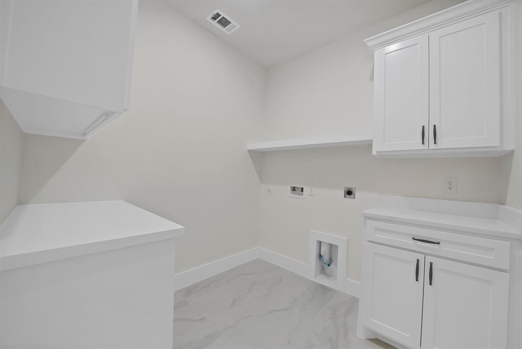 Laundry area featuring white shaker-style cabinetry, solid-surface countertops, large-format tile flooring, and integrated shelving