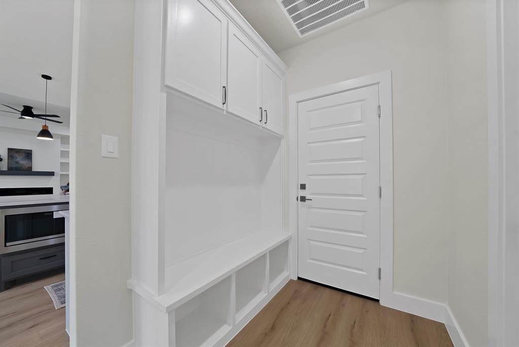 Built-in white cabinetry featuring upper storage lockers and lower open cubbies, paired with a classic five-panel door and wood-finish flooring