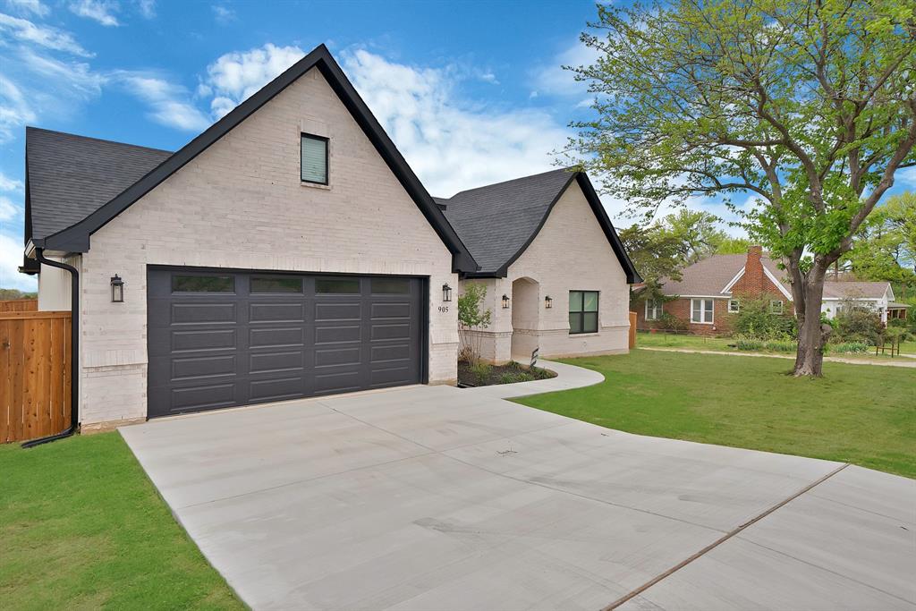 Light-colored brick exterior featuring high-pitched rooflines, a multi-car garage with dark finish paneling, and a paved concrete driveway
