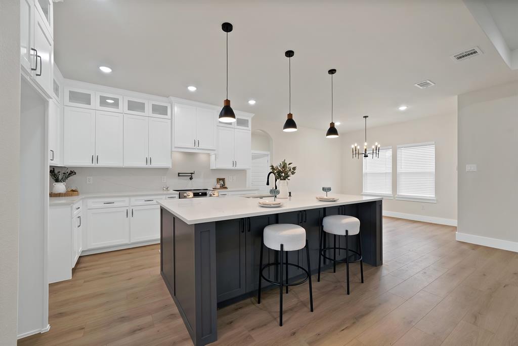 Kitchen featuring white shaker-style cabinetry with glass-front uppers, quartz countertops, a contrasting dark-finish center island, wood-finish flooring, and recessed and pendant lighting