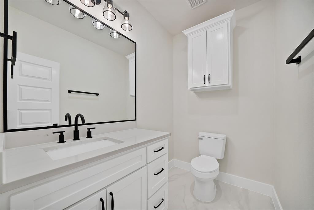 Bathroom featuring a white vanity with a quartz countertop, an integrated rectangular sink, black matte hardware, a wall-mounted storage cabinet, and an oversized framed mirror