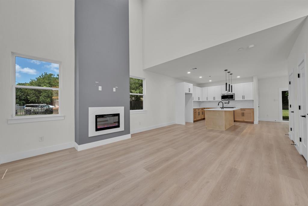 High-ceiling living area featuring wood-finish flooring, a full-height gray accent wall, and a built-in fireplace with a white surround