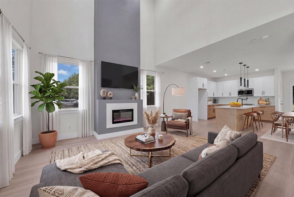 Double-height ceilings, floor-to-ceiling fireplace feature wall with integrated hearth, wood-finish flooring, kitchen island with built-in cabinetry, and pendant lighting